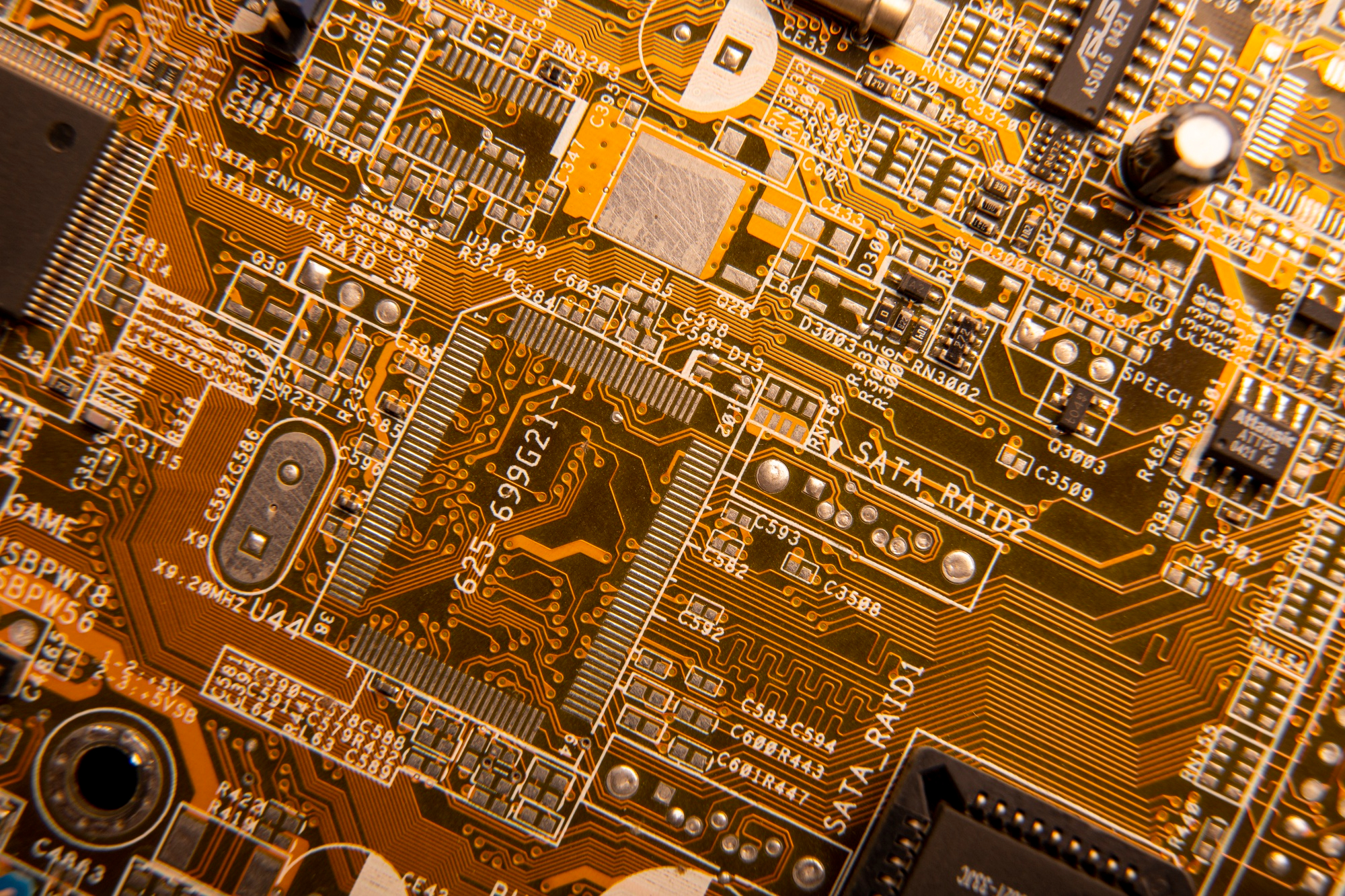 A detailed close-up of a computer circuit board, highlighting its orange and gold traces.